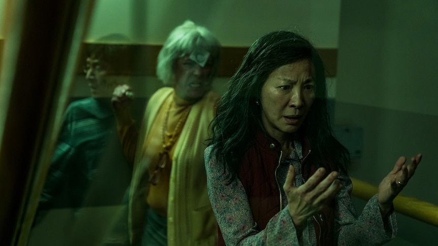 模糊的绿色调镜头，一位困惑的中国长发女性；背景中的亚洲男人和白人女人。